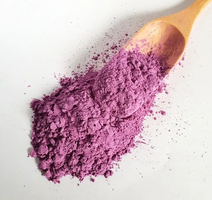 Purple ube barista powder in a small white spoon on a light concrete surface, overhead view