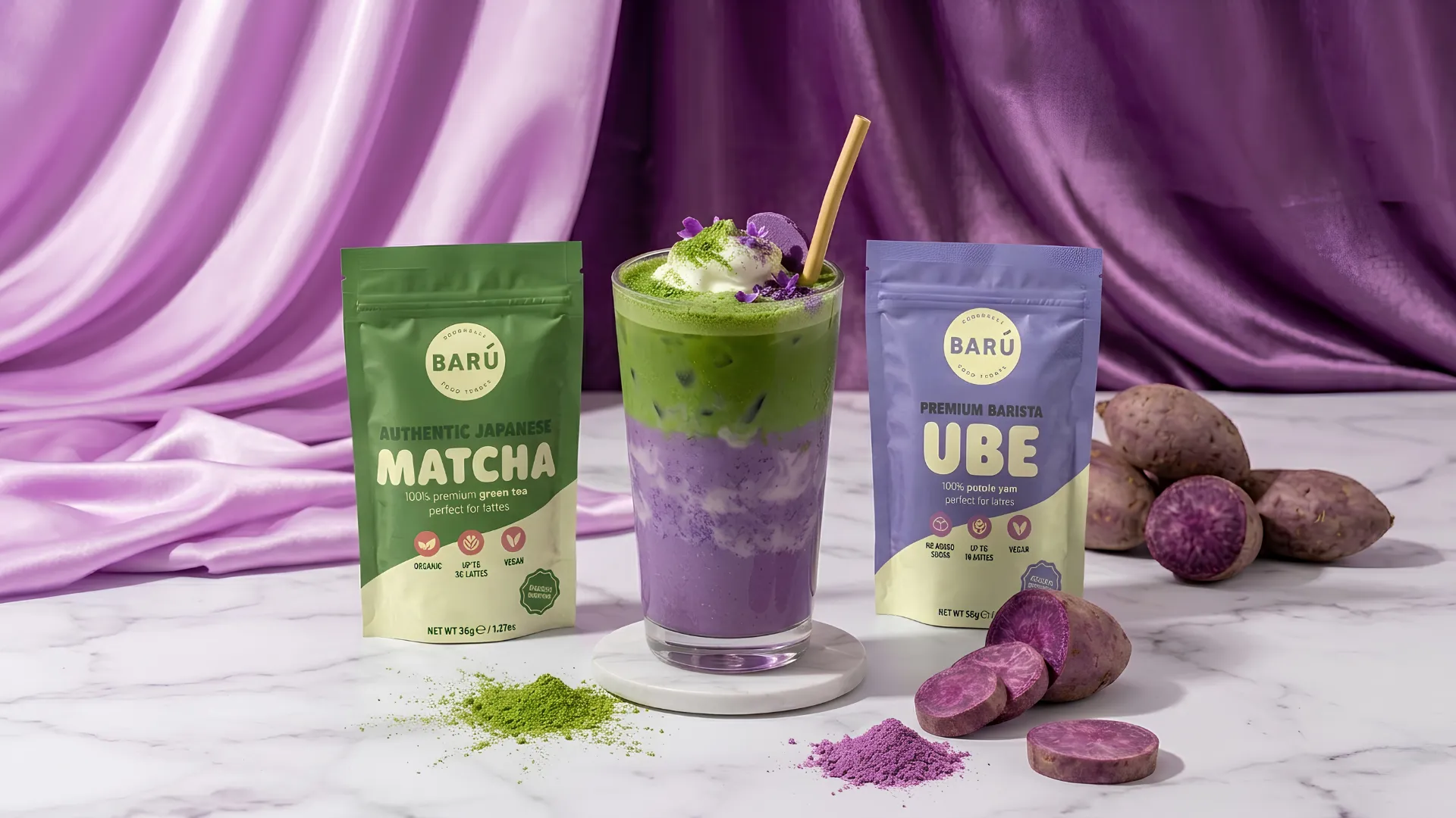 Ube barista powder and matcha powder packets beside a layered ube matcha latte in a clear glass, with fresh purple yam pieces and green matcha powder on a marble surface