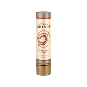 Monin L'Artiste caramel flavoured sauce in 150ml cylindrical tube with cream label, warm amber swirl motif and rust-orange accent bands, on white background